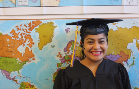 graduate smiling for picture with map of the world in the background