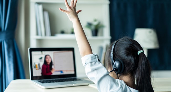 Student with headphones raising hand while learning virtually on a laptop