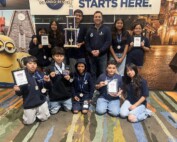 Students standing and kneeling on the floor with certificates and a trophy